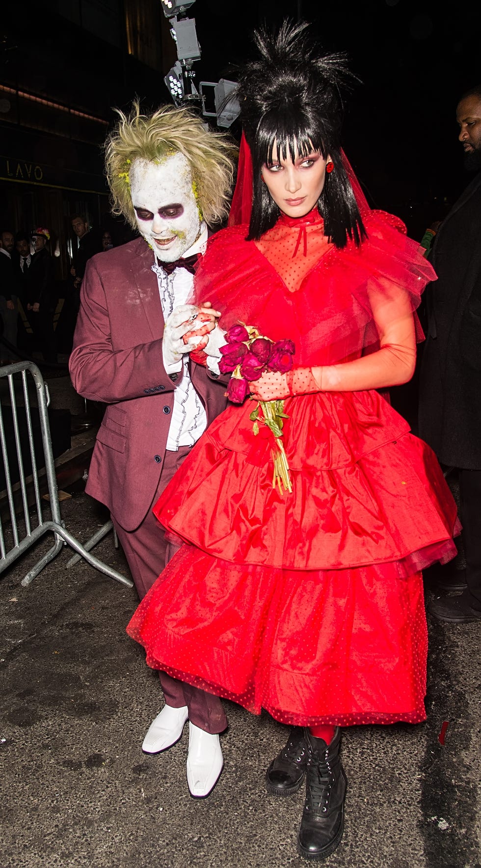 couples costumes, a man wearing white ghost beetlejuice makeup and suit and a woman in a red bride dress with a black wig and red flowers