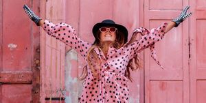 model in pink polka dot dress and gloves with black hat in london jumping of happiness