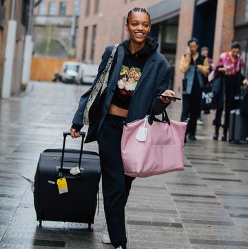een model met roze shopper en koffer op straat