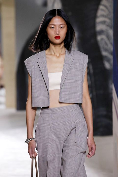 a model wearing a strapless white baneau top and grey vest on the hermes runway in a roundup of the best strapless bras for small chests 2023