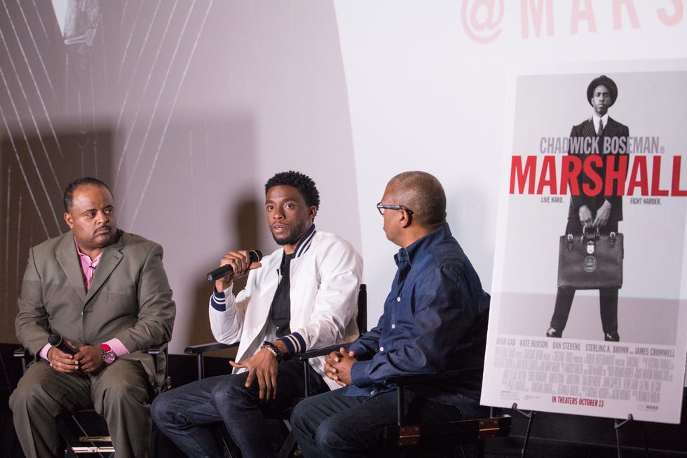 two men sit in chairs on either side of chadwick boseman, who also sits and speaks into a microphone