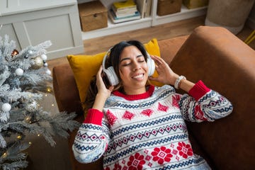young woman laying down on the couch next to a christmas tree listening to music through headphones