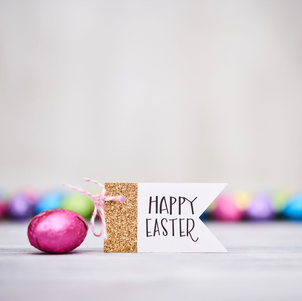 modern easter background with foil covered chocolate easter candy and a sign reading happy easter