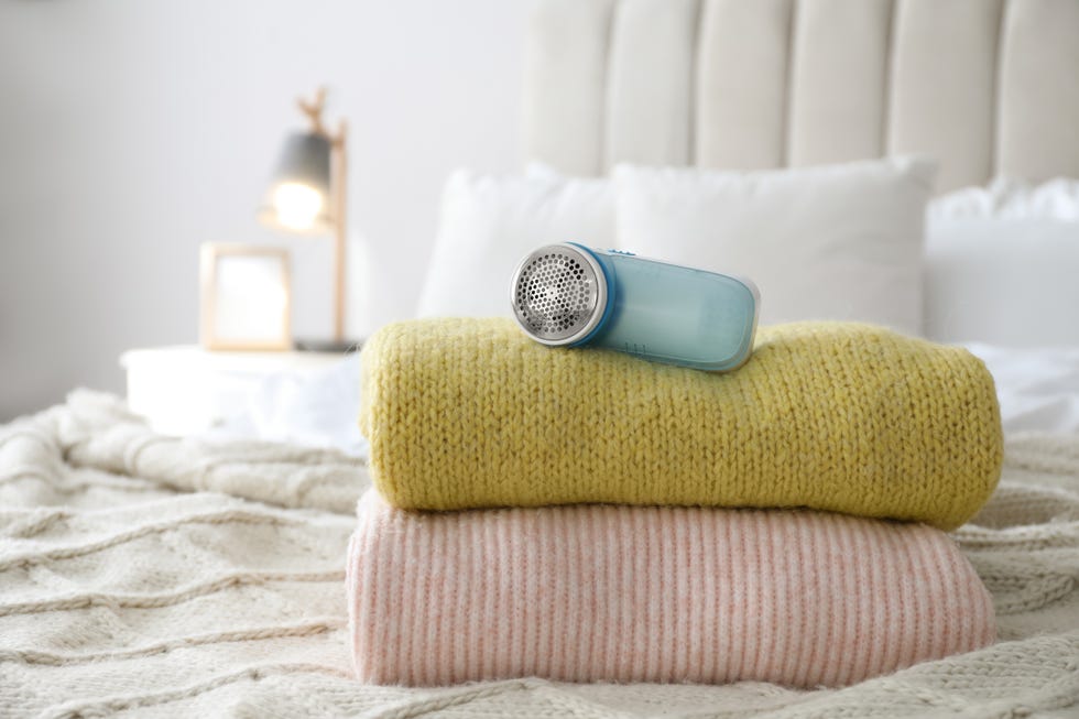 modern fabric shaver and woolen sweaters on bed indoors