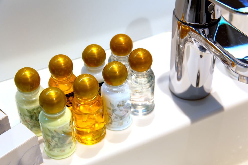 modern faucet and ceramic sink in bathroom vials with various shampoos and oils