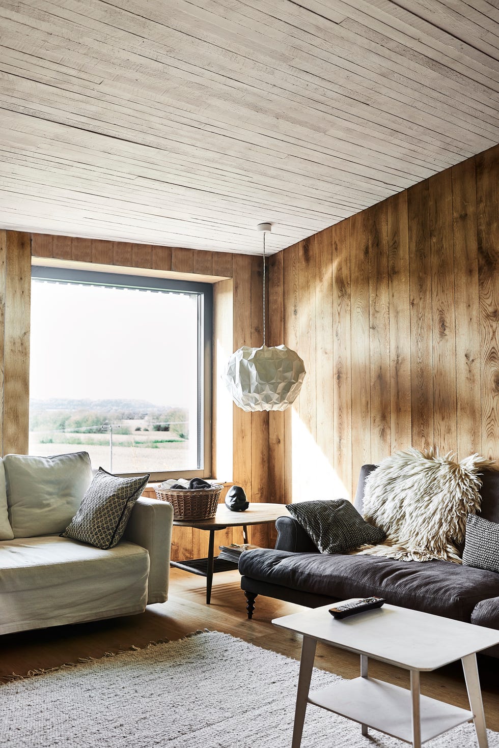 a timber clad snug with a white and grey sofa, paper pendant lampshade, and chunky white rug