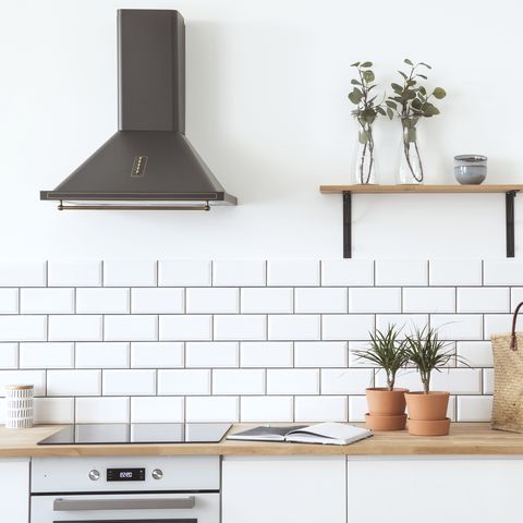 Modern scandinavian open space with kitchen accessories, plants, wooden shelf, and straw bag . Design room with white brick walls.