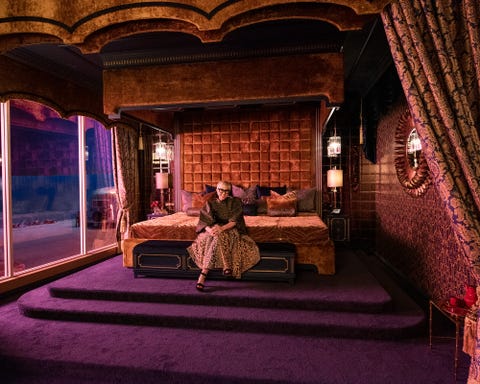 a blonde woman with glasses and leopard print skirt sits on a bed with gold pillows and a gold tiger striped bedspread