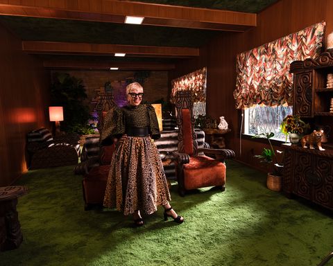 a blonde woman with a leopard print skirt stands in a wood paneled room with green carpet