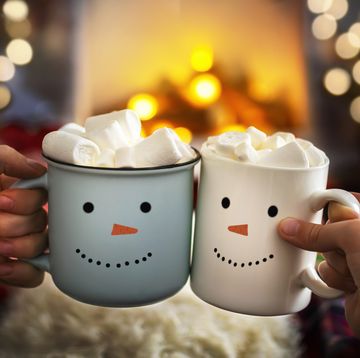 mom and child are relaxing together on a cozy winter evening by the fireplace, close up of two hands with snowman face cup of hot cocoa with marshmallows christmas holidays, happy moments at home
