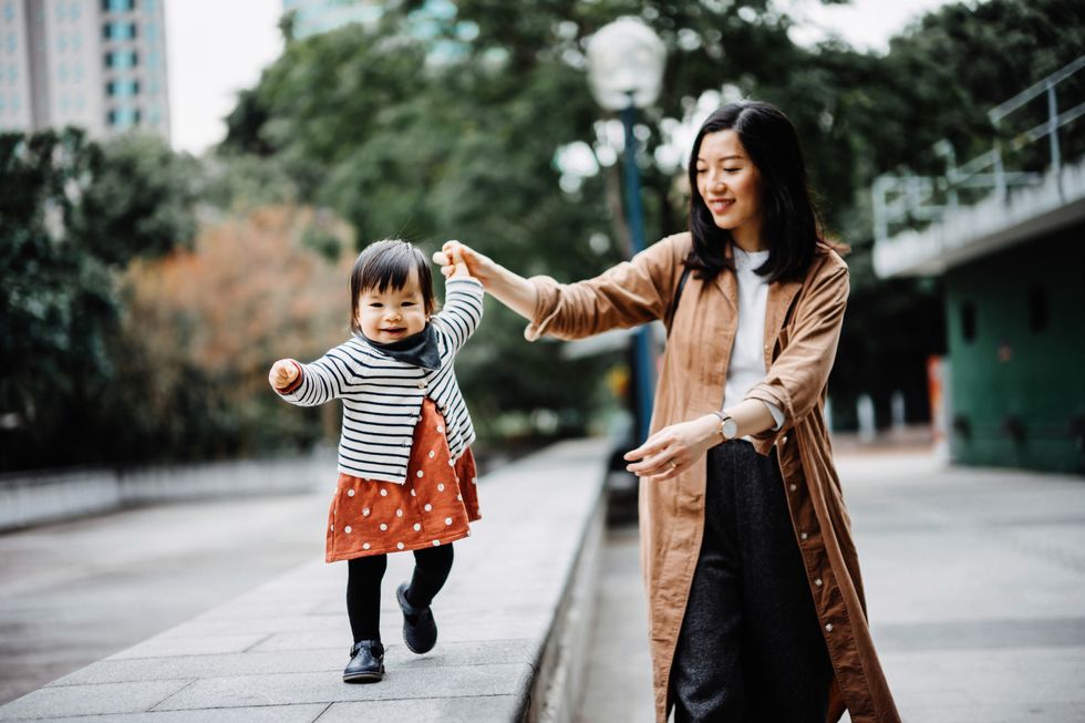 joyful toddler girl strolling in the park while holding hand in hand with mother, both of them are enjoying family time