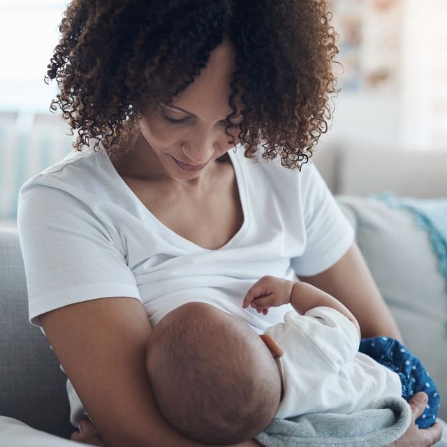 young black woman sitting on a couch breastfeeding her baby