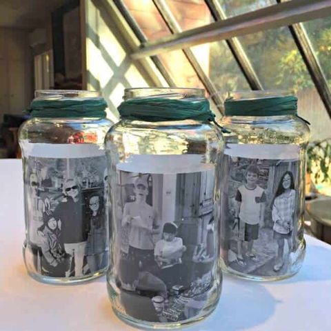three jars sitting on a table with a white tablecloth each jar has green ribbon around the top curled inside of each jar is a black and white family photo