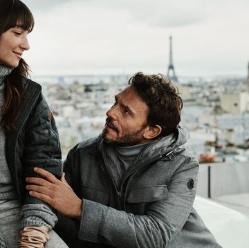 a man and woman sitting on a rooftop overlooking a city