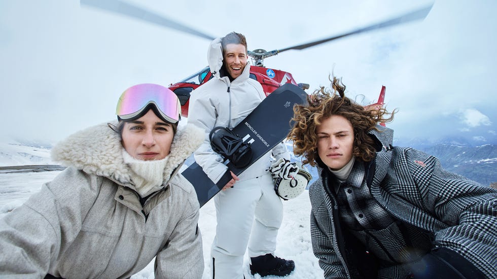 group of snowboarders at a snowy location with a helicopter in the background