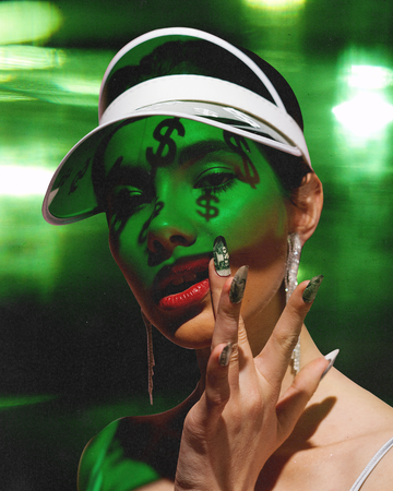 a woman in green light with dollar signs shadowed on her face and dollar bill nail art