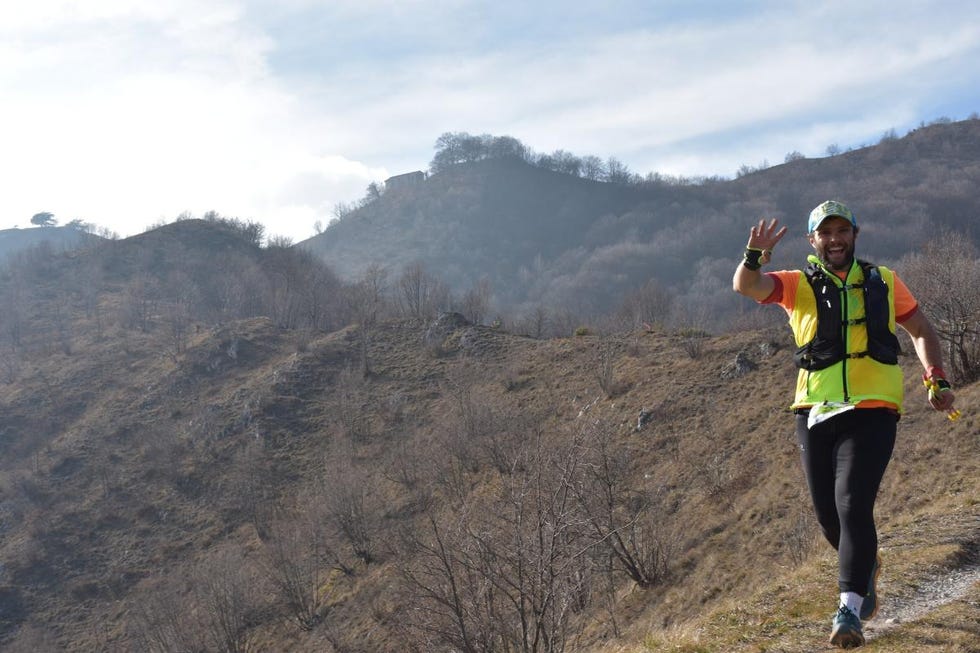 a runner on a mountain trail waves surrounded by a landscape of hills and sparse trees