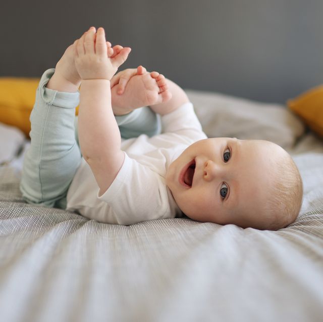 a 6 month old baby boy smiling, laying on a bed