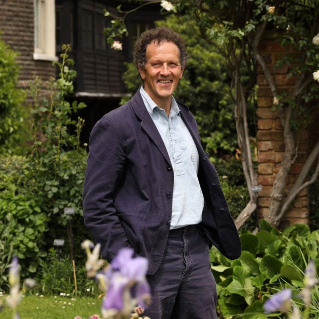 a man dressed casually stands in a garden