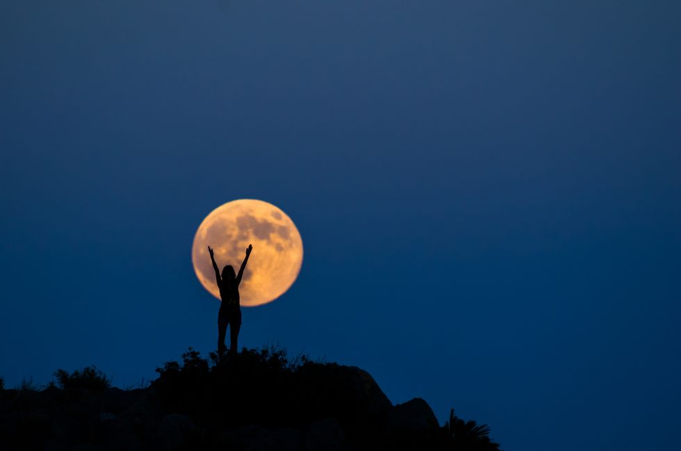 happy silhouette with arms raised on the full moon woman the years biggest moon, in benicassim, castellon