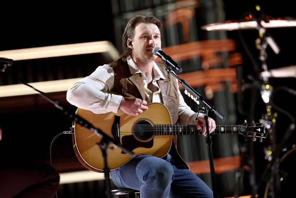morgan wallen playing guitar and singing while sitting on a stool for a stage performance