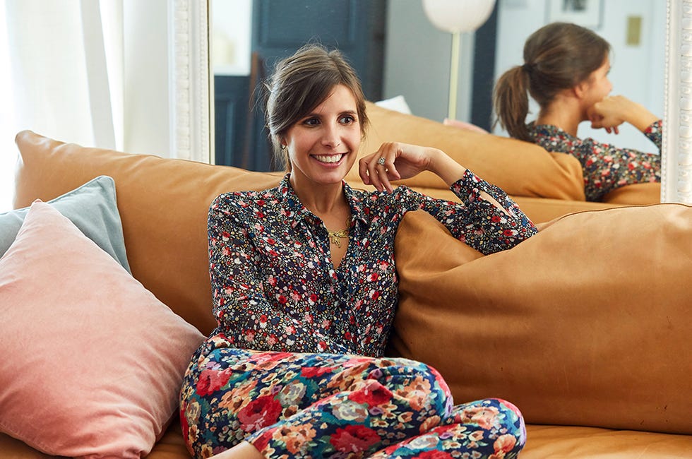 morgane sealory of sezane sits on a couch wearing a floral blouse and contrasting floral pants