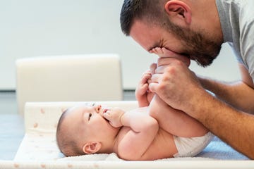 a dad cuddles his baby's feet after treating the baby with diaper rash cream and putting on a fresh diaper