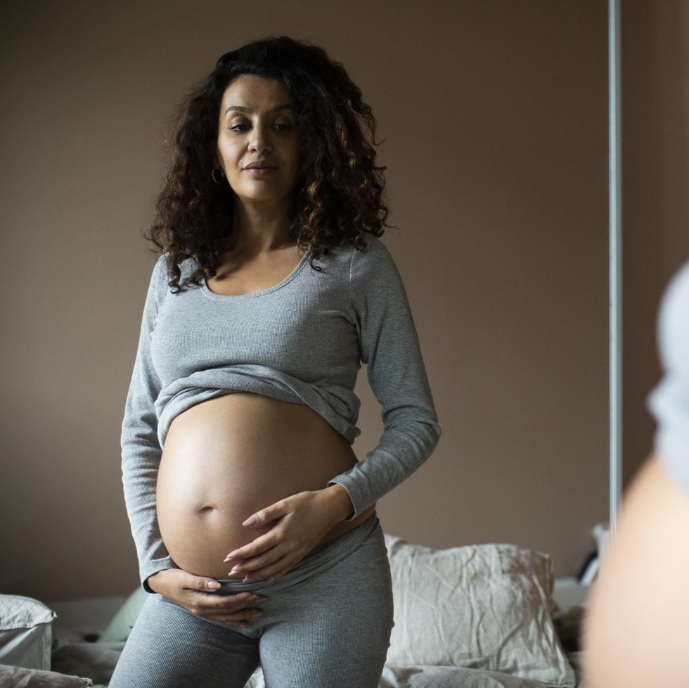 pregnant woman looking in mirror at her bump while at home