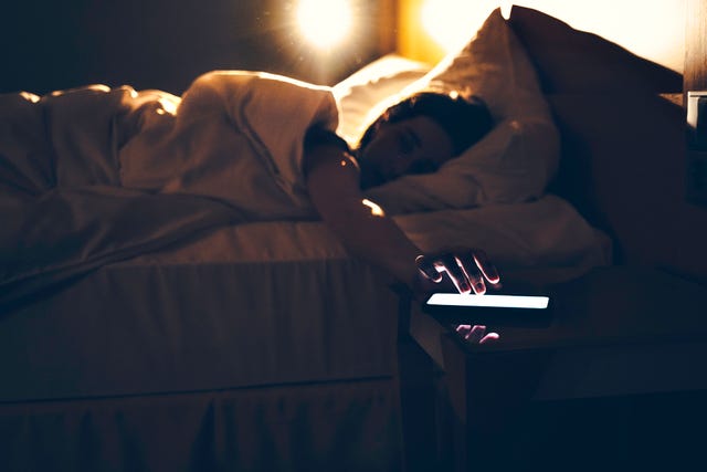 morning shot of a person lying in bed tapping phone, turning off the alarm