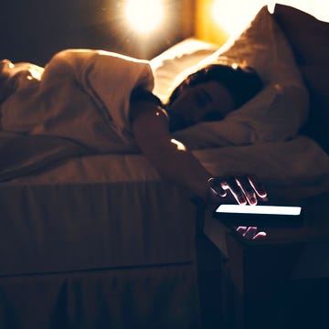 Morning shot of a person lying in bed tapping phone, turning off the alarm morning shot of a person lying in bed tapping phone, turning off the alarm
