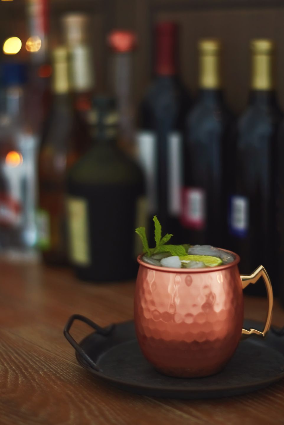 moscow mule drink in a copper mug with an assortment of bottles of alcohol in the background