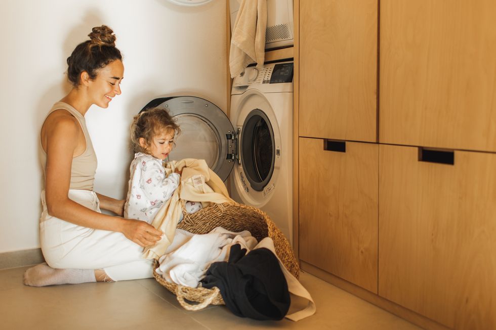 mother and daughter loading washing machine with laundry together sustainable parenting