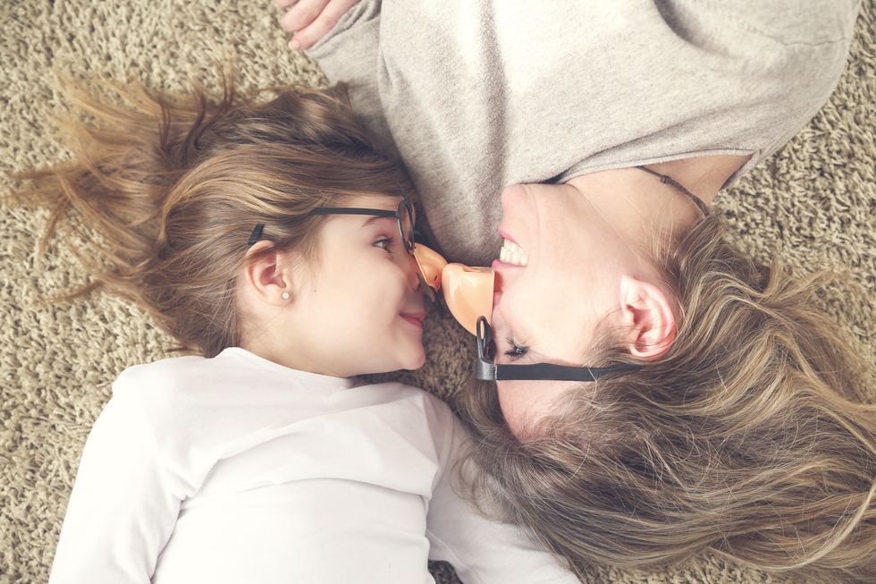 mother and daughter lying on the carpet wearing funny glasses with plastic nose
