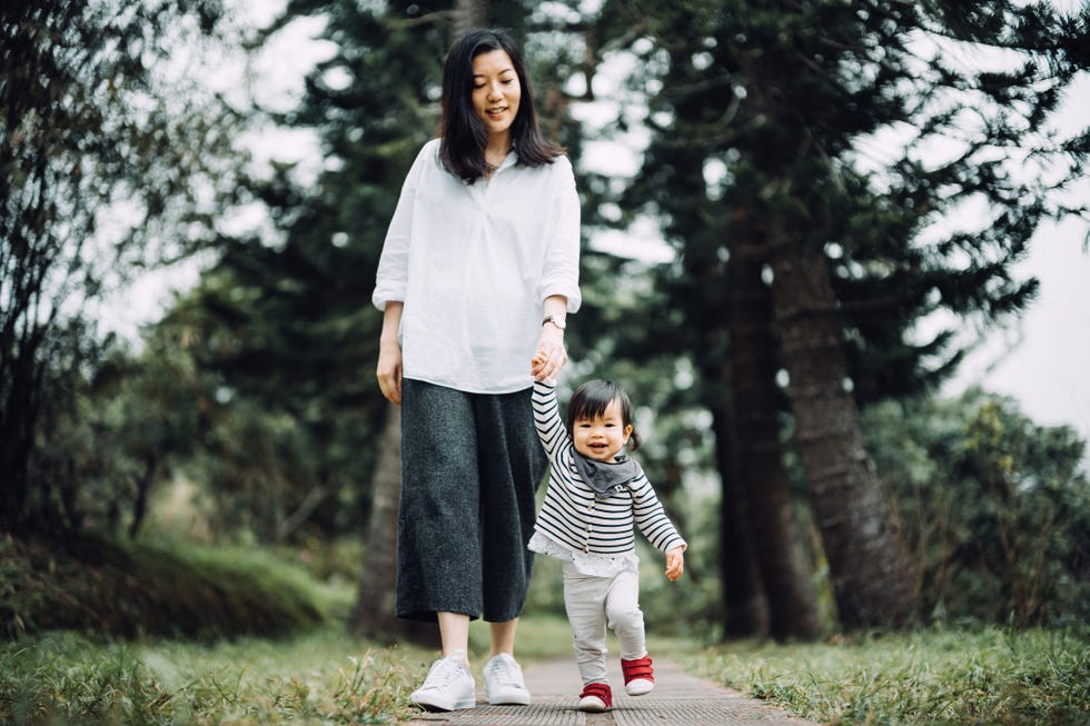 mother and toddler girl walking hand in hand along the pathway in the nature park, they are having a great time and smiling joyfully