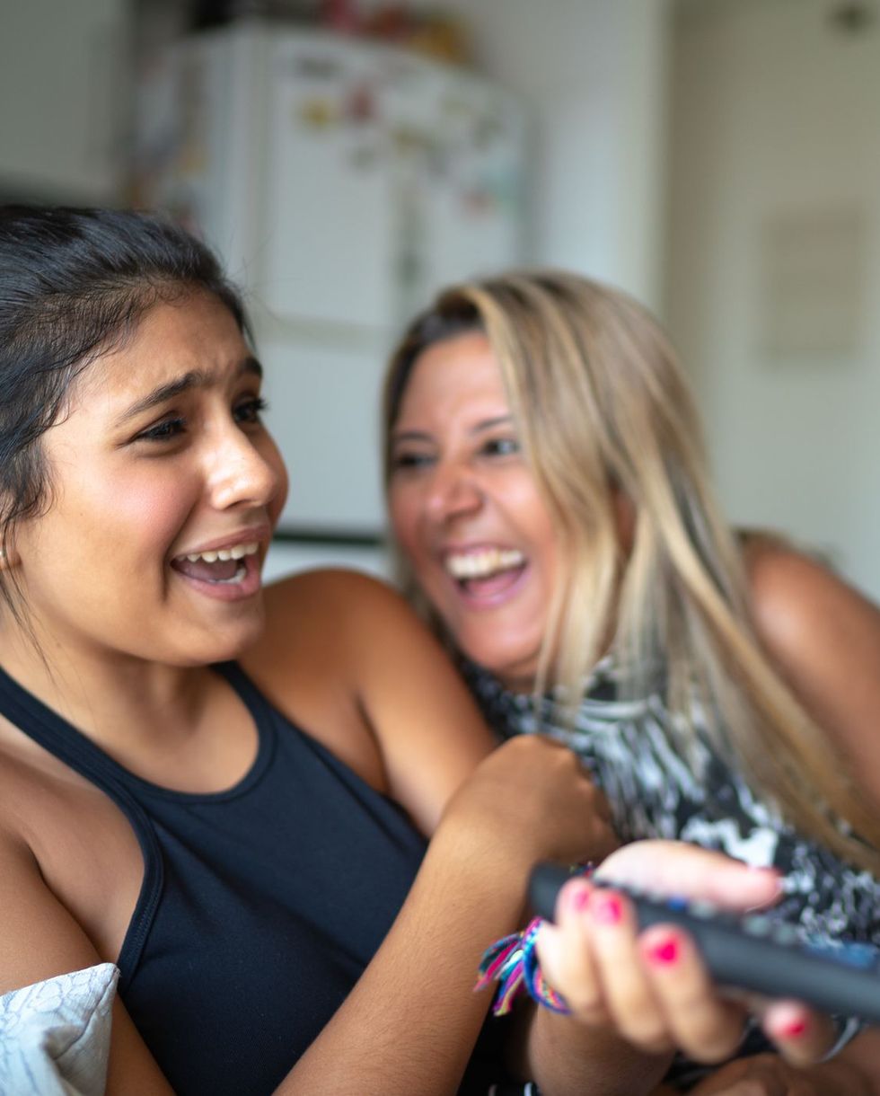 mother and teen daughter watching tv together, laughing