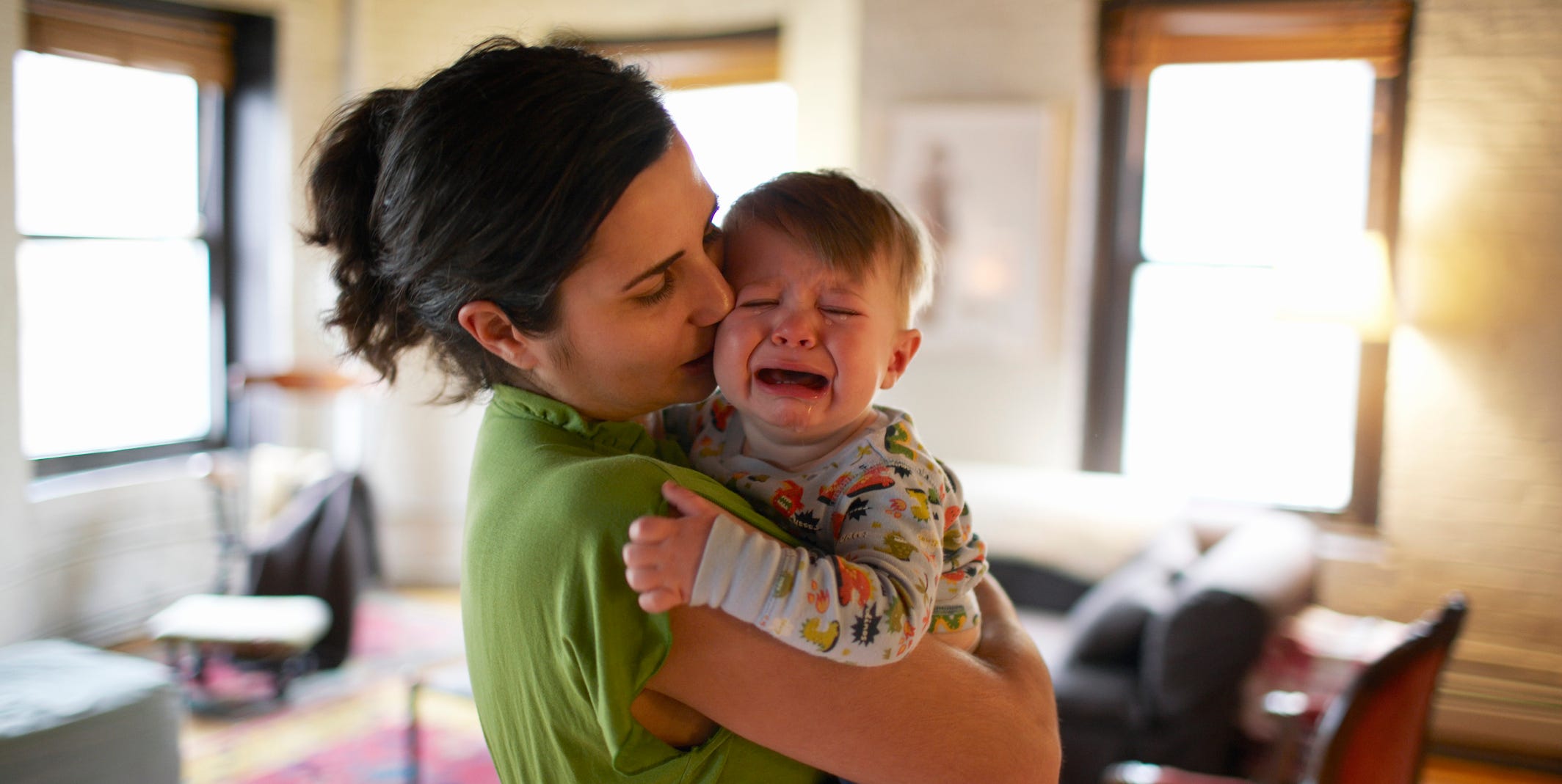 mother holding and kissing crying baby boy 12 17 months focus on foreground