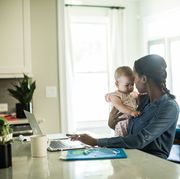 mother holding baby while using laptop working from home