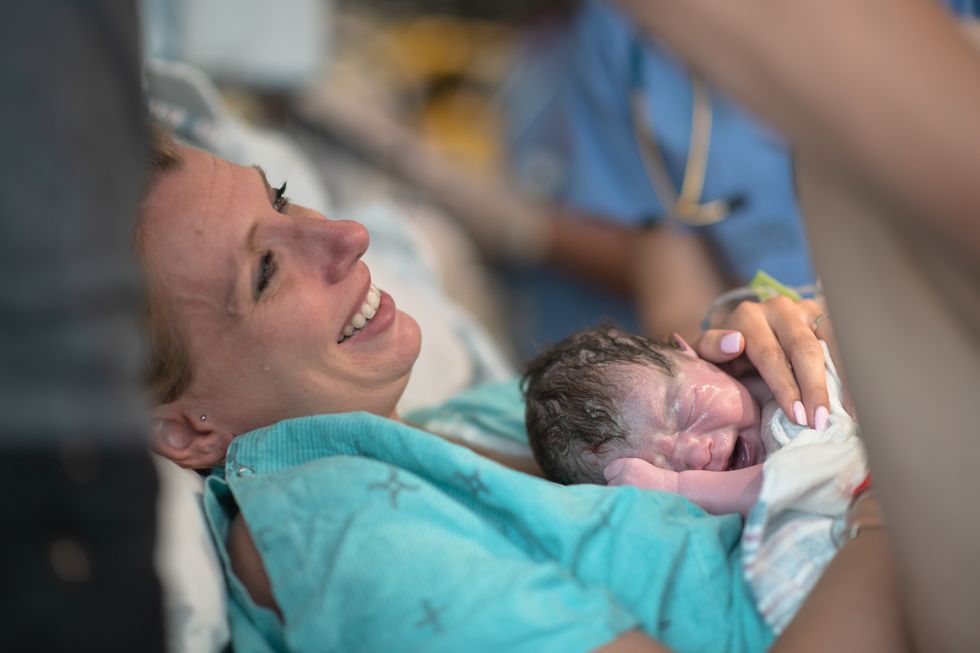 una mujer, muy emocionada, con su bebé recién nacido en brazos tras el parto
