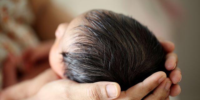 las manos de una mujer sostienen la cabeza de un recién nacido con mucho pelo
