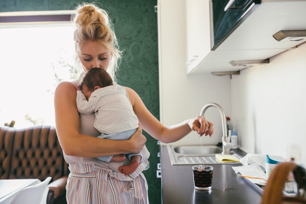 mother holding newborn baby in kitchen while making tea