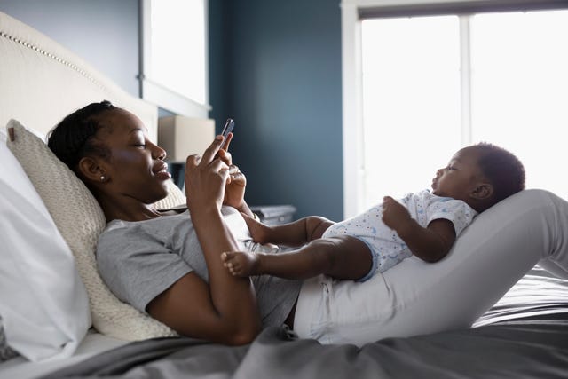 Mother with camera phone photographing baby son in lap on bed