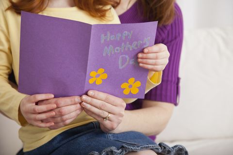 Mother with daughter (4-5) holding Mother's Day card together, midsection