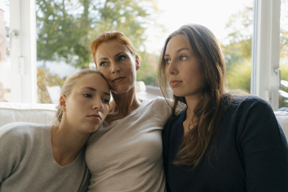 Mother with two teenage girls relaxing on couch at home