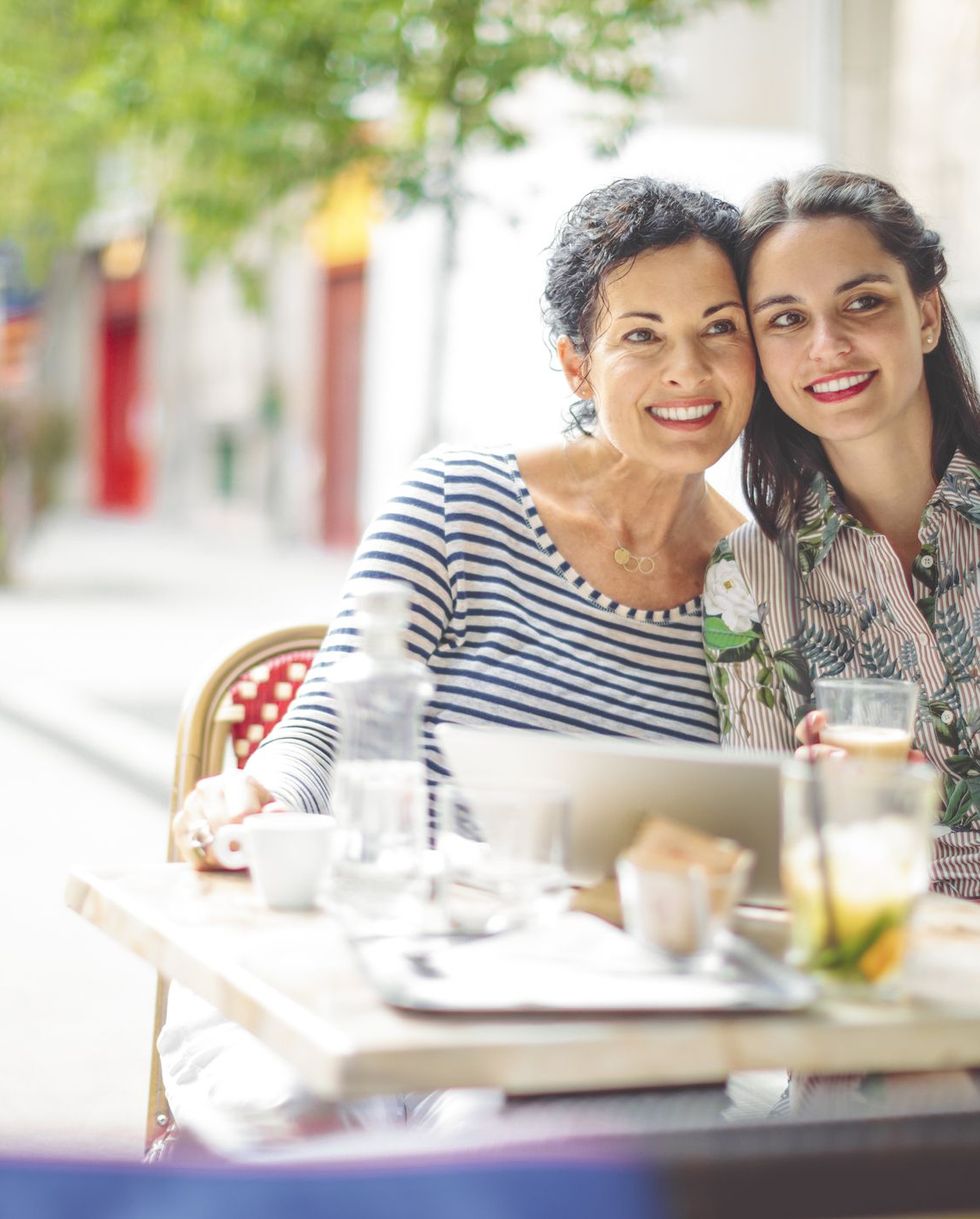 mother and adult daughter are taking selfies at an outdoor cafe, possibly at a mother's day brunch