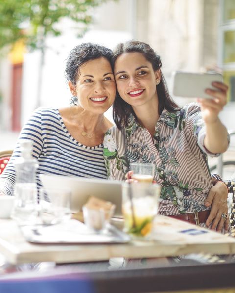 mother and adult daughter are taking selfies at an outdoor cafe, possibly at a mother