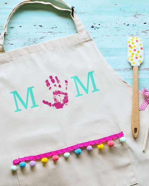 apron with child's handprint as the letter o in mom with colorful pompom fringe that you can make as a mother's day activity