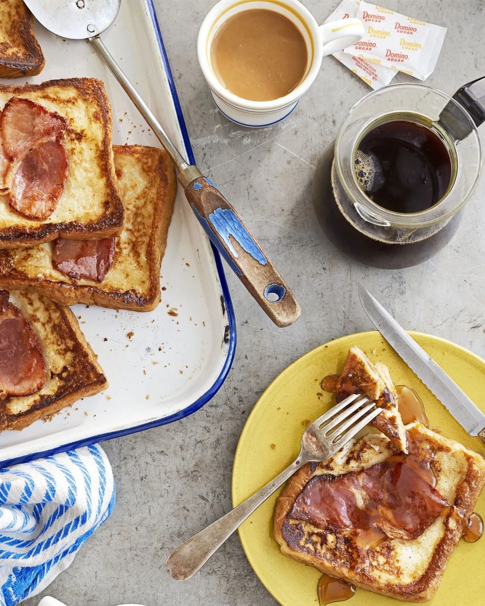 country ham covered french toast on a yellow plate with cups of coffee and sugar packets strewn about