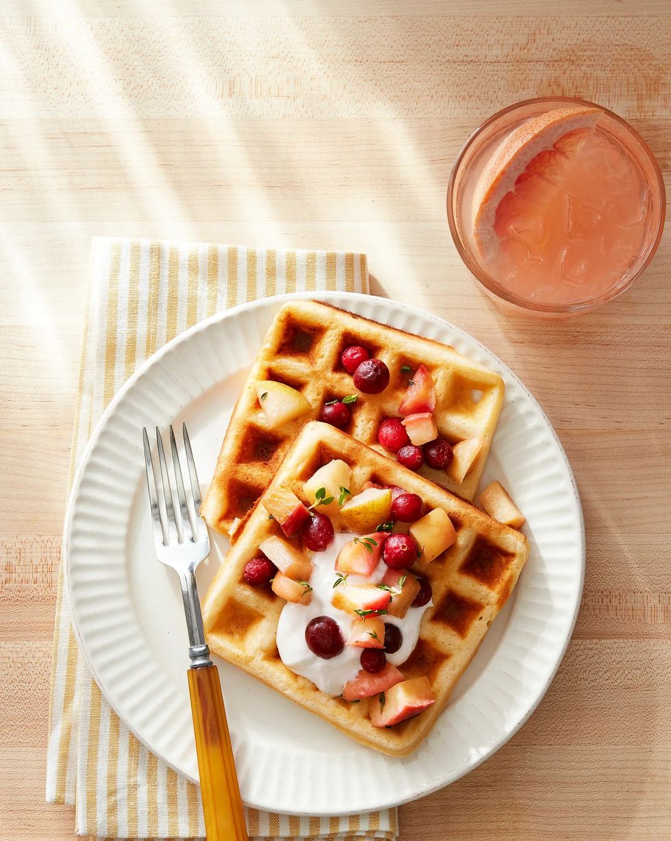 overnight yeasted waffles covered with fruit compote and yogurt, on a plate with a grapefruit cocktail on the side
