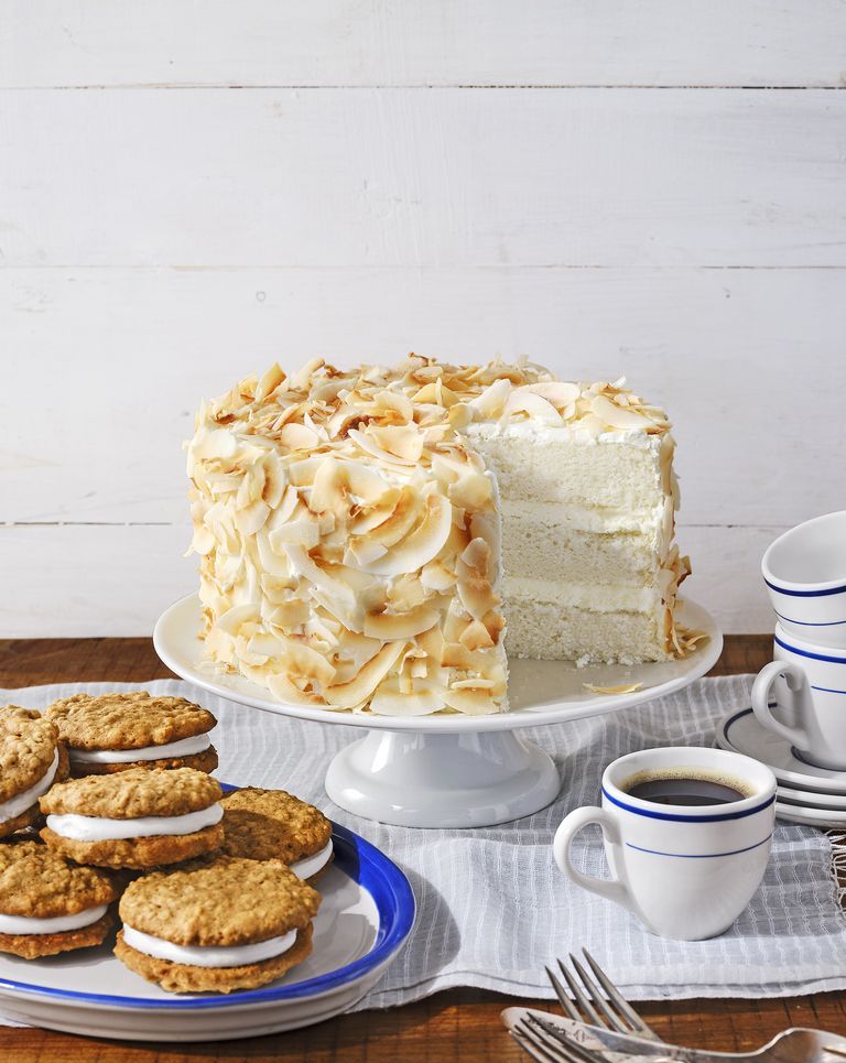 three layer angel coconut cake covered in toasted coconut flakes on a white cake stand