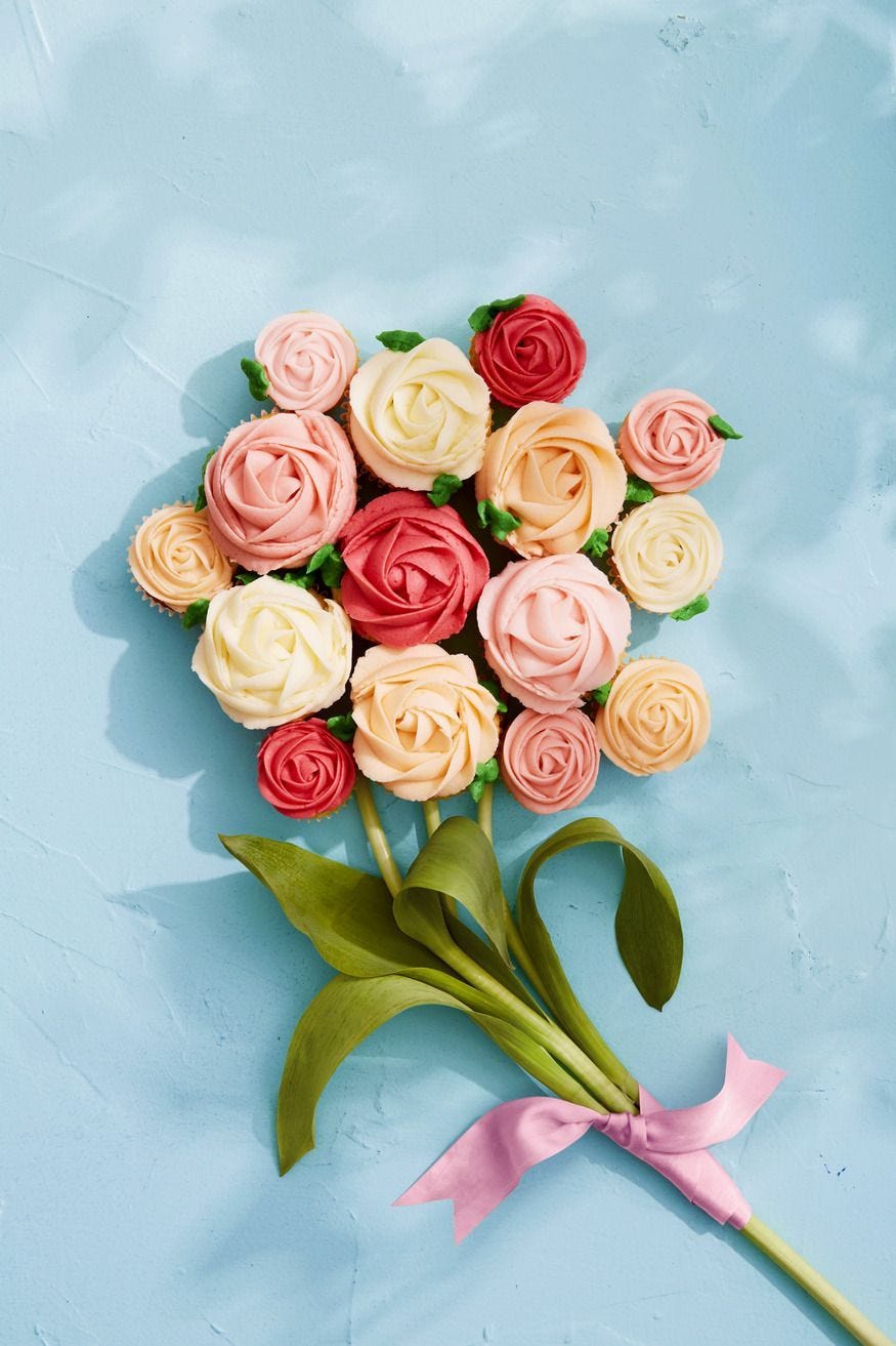 vanilla buttercream cupcakes with frosting piped like roses and arranged like a bouquet with real flower stems